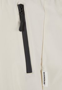 Pantaloni da esterno beige chiaro con una tasca con zip nera e un'etichetta cucita con il nome del marchio sul lato. Tessuto liscio e leggero.