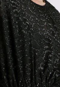 Robe noire avec un tissu texturé présentant un motif abstrait brillant. Le design comporte des accents irisés dispersés sur toute la surface.