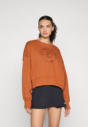 Rustfarget hettegenser med en cropped design, med et rundt logo i midten, kombinert med et svart skjørt. Myk, teksturert stoff.