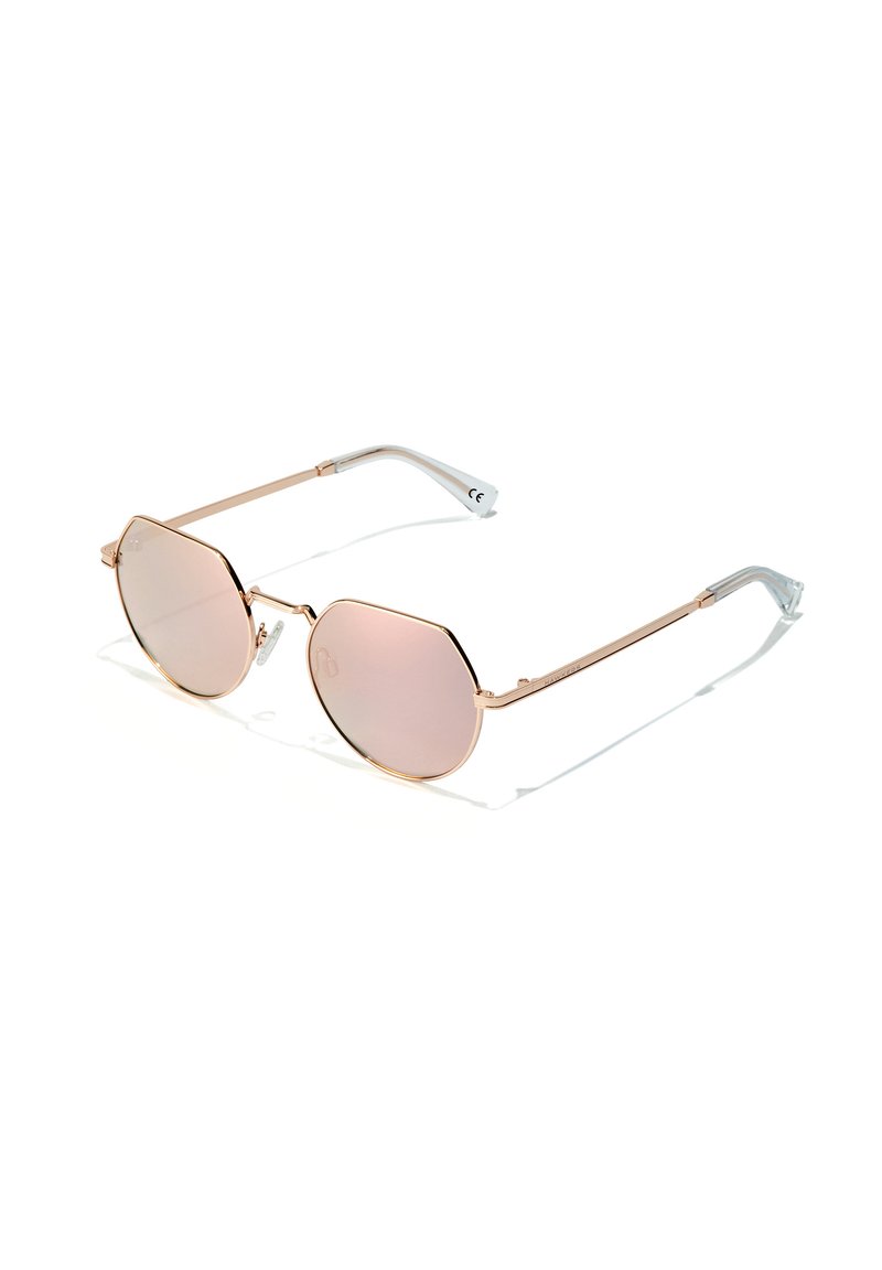 Gafas de sol de metal dorado con lentes octagonales de tono rosa y acentos en las patillas transparentes; presentan brazos delgados y un diseño minimalista.