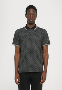 Polo noir avec un motif de logo gris répétitif, col et poignets assortis accentués de rayures blanches.