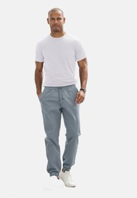 Grijze katoenen joggingsbroek met een elastische tailleband en boorden, gedragen met een eenvoudig wit T-shirt met ronde hals en witte sneakers.