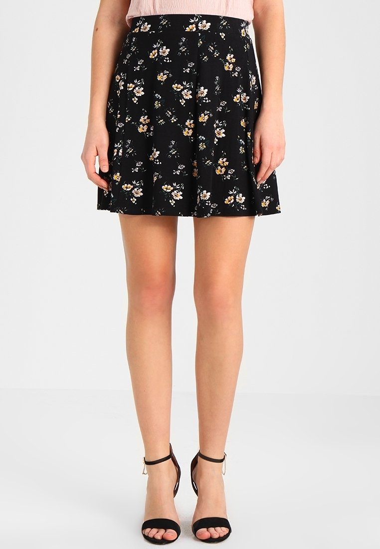 Jupe florale noire avec un design plissé, ornée de petites fleurs jaunes et blanches. Tissu léger avec une forme évasée, longueur au-dessus du genou.
