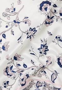 Λευκό ύφασμα με μπλε και ανοιχτό ροζ λουλουδάτο σχέδιο, απαλές πτυχές δημιουργούν απαλά σκιάσεις στην επιφάνεια.