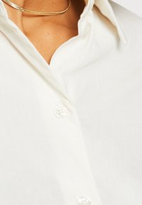 Col et boutons d'une chemise blanche avec un collier chaîne en or visible autour du cou d'une personne.