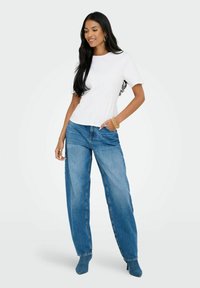 Vit kortärmad t-shirt med rund halsringning, matchad med ljusblå vida jeans, som har en avslappnad passform och lätt slitna detaljer.
