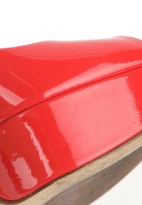 Gros plan d'une chaussure à talon haut rouge brillante montrant la partie supérieure courbée et la semelle beige usée.