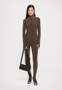 Brown, long-sleeve bodysuit in a fitted design, paired with a black handbag and open-toed black heels, worn by a model with long hair.