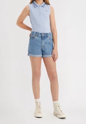 Jasnoniebieska bezrękawnikowa polo z dwoma ciemnymi paskami na kołnierzu, zestawiona z podwiniętymi szortami jeansowymi. Białe, sznurowane trampki za kostkę.