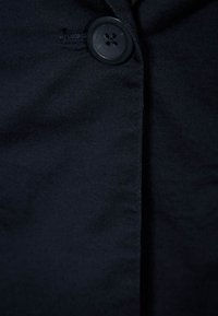 Navy blue fabric with a smooth texture featuring a single black button near the seam, highlighting a simple garment design.
