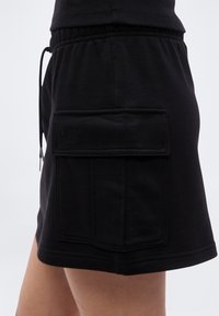 Μαύρη φούστα μεσαίου μήκους από μαλακό ύφασμα, με πλαϊνή τσέπη και ελαστική μέση με κορδόνι. Διακριτική λεπτομέρεια με κεντημένο λογότυπο.