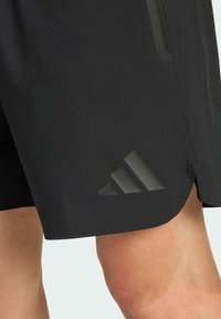 Pantalones cortos deportivos negros con una textura suave, que presentan un logotipo reflectante de tres rayas en el dobladillo y un detalle de bolsillo con cremallera.