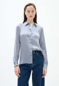 Randig blå och vit långärmad skjorta med knapp-down krage, slät textur och knapprad. I kombination med högmidjade blå jeans.