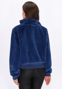 Giacca in pelliccia sintetica blu con colletto alto e polsini a costine, caratterizzata da una vestibilità comoda e una texture liscia.