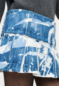 Μίνι φούστα από τζιν με πιέτες σε αποχρώσεις του μπλε και λευκού, με αφηρημένα μοτίβα, συμπληρωμένη από φαρδιά μέση και διακοσμητικές ραφές.