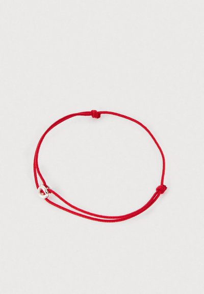 Braccialetto regolabile in corda rossa con un piccolo ciondolo a forma di cuore in argento su uno sfondo grigio chiaro.
