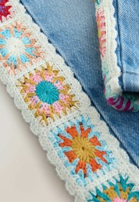 Gros plan sur des carrés floraux multicolores au crochet cousus sur le bord d'un tissu en denim bleu.