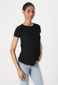 Camiseta negra de manga corta con textura de canalé y bordes en forma de ondas, con un corte relajado. Combinada con jeans de color azul claro, mostrando una textura suave.