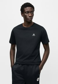 Μαύρο βαμβακερό t-shirt με στρογγυλή λαιμόκοψη και κοντά μανίκια, με μικρό λευκό λογότυπο Converse στην αριστερή πλευρά του στήθους.