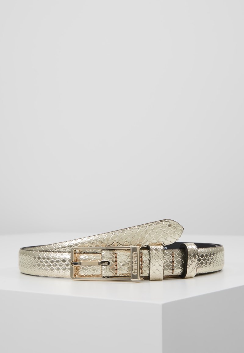 Ceinture métallique dorée avec motif serpent en relief, boucle rectangulaire dorée et deux passants sur une surface blanche.