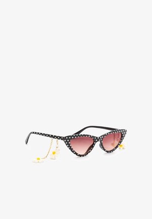 Czarne okulary przeciwsłoneczne w kocim stylu z białymi kropkami, różowymi soczewkami z gradientem i zwisającymi białymi zawieszkami w kształcie stokrotek na złotych łańcuszkach.