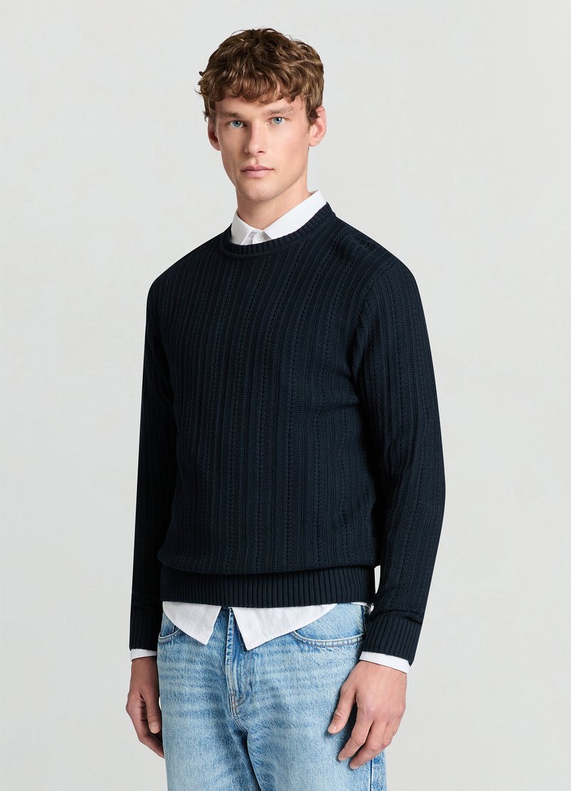 Maglione blu navy a maglia con trama a coste, scollo rotondo e maniche lunghe, indossato sopra una camicia bianca con colletto. Vestibilità classica, stile casual.
