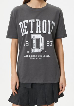 Osoba nosząca ciemnoszarą koszulkę z napisem „DETROIT 1987”, dużą zniszczoną literą „D” oraz tekstem „Conference Champions Doing My Best.”