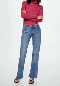 Pull à col roulé rouge associé à un jean droit bleu clair. Le jean présente une texture denim classique et un design à cinq poches. Des sandales noires à brides complètent la tenue.