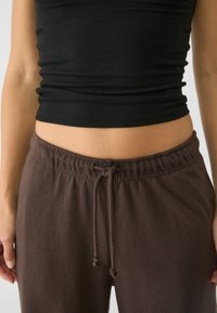 Czarny prążkowany crop top w połączeniu z brązowymi spodniami dresowymi z troczkiem. Spodnie mają elastyczny pas i miękki, fakturowany materiał.