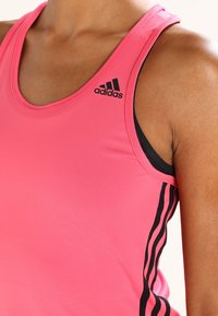 Różowy sportowy top na ramiączkach z czarnymi akcentami i trzema paskami po bokach. Wykonany z gładkiego, elastycznego materiału, z logo adidas.