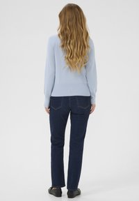 Maglione aderente di colore azzurro chiaro con maniche lunghe, abbinato a jeans dritti blu scuro. La vista posteriore mostra il tessuto strutturato e i dettagli delle cuciture.