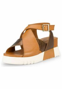 Sandale en cuir marron avec des lanières croisées, bout ouvert, boucle à la cheville, et une épaisse semelle blanche avec un léger talon. Accents métalliques inclus.