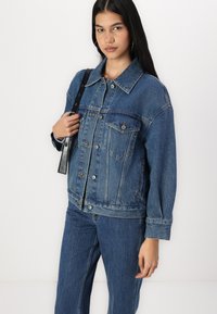 Jeans jakna u plavoj boji s klasičnim dizajnom, s srebrnim hardverom, dva džepa na grudima i opuštenim krojem. Tkanina ima teksturiranu završnu obradu.