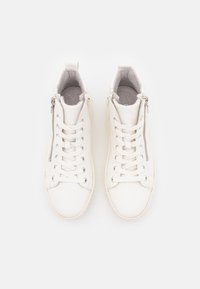 Białe sneakersy za kostkę z sznurowadłami i zamkami błyskawicznymi po bokach, pokazane z góry na jednolitym białym tle.