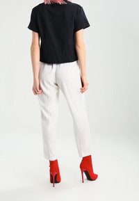 Svart kortärmad t-shirt, vita vertikala randiga byxor och röda högklackade ankelstövlar. Slät tyg med en figurnära design och skräddarsydd passform.