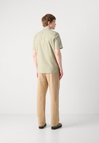 Camisa de manga corta verde claro con cuello recto, combinada con pantalones de pierna ancha beige y zapatos oscuros. Diseño sencillo, sin patrones visibles.