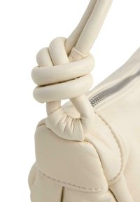 Borsa a mano in pelle crema con manico annodato, caratterizzata da una texture liscia e dettaglio della cerniera metallica lungo il lato.