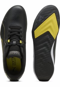 Schwarze Sportschuhe mit gelben Akzenten. Glattes synthetisches Obermaterial, perforiertes Design, abgerundete Zehenpartie, profilierte Gummisohle mit Logo.