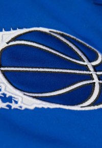 Ein blauer Stoff zeigt ein weißes und schwarzes, gesticktes Basketballdesign, das durch eine strukturierte Naht und einen eleganten, sportlichen Stil akzentuiert wird.
