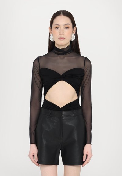 Haut noir à manches longues en tissu en maille transparente, avec un design découpé à la taille. Associé à un short en cuir noir et de grandes boucles d'oreilles.