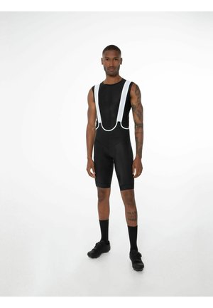 Sort cykeloutfit med hvide stropper, lavet af åndbart materiale. Tætsiddende design, korte ben og synlige ankellange sorte sokker.