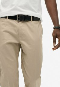 Chinos beige con una textura suave, un cinturón de cuero negro con una hebilla de metal plateada, llevados con una camiseta blanca lisa.