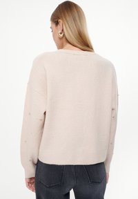 Hellrosa gestrickter Pullover mit lockerer Passform, breitem Ausschnitt und Perlenverzierungen an den Ärmeln. Weiche Textur, cropped Design.