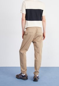 Beiga joggerbyxor med elastiska muddar och två bakfickor, kombinerade med en krämvit och svart randig t-shirt samt bruna träningsskor.