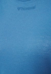 Modrá sportovní košile vyrobená z prodyšné tkaniny, s texturovaným vzorem a vyraženým logem na výstřihu.