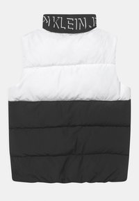 Prošívaná vesta v černé a bílé barvě s vysokým límcem. Má prošívaný vzor a pás s logem u výstřihu. Měkký, izolovaný materiál.