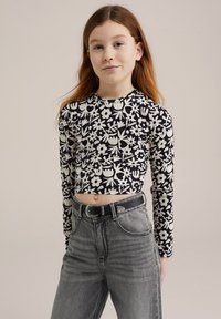 Fekete-fehér, hosszú ujjú crop top virágmintával, magas derekú szürke farmernadrággal és fekete övvel, amely ezüst csattal díszített.