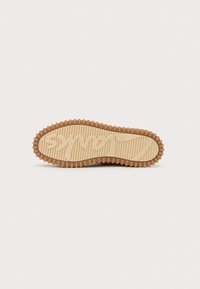 Rubber sneaker sole with a textured, ridged pattern in light tan. Features a prominent logo design and circular edge for grip.