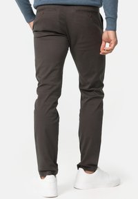 Tummanruskeat chinot kapealla istuvuudella, joissa on kaksi takataskua napituksella ja sileä pinta. Yhdistetty valkoisiin tennareihin.