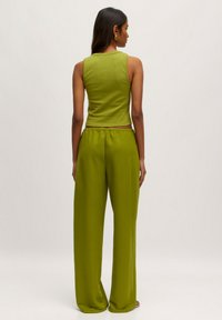 Grünes ärmelloses Oberteil und passende weite Hosen, beide aus einem weichen Stoff. Das Oberteil hat einen runden Ausschnitt und die Hosen verfügen über einen elastischen Bund.